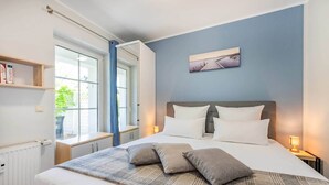 A bedroom with a bed, bedside tables, a window, a radiator, and a wall-mounted picture. - Comfortable vacation apartment in Koserow with terrace and modern furnishings (Koserow)