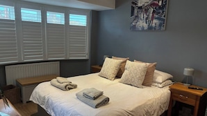 Une chambre avec un grand lit, un tableau au mur et une fenêtre avec des stores.