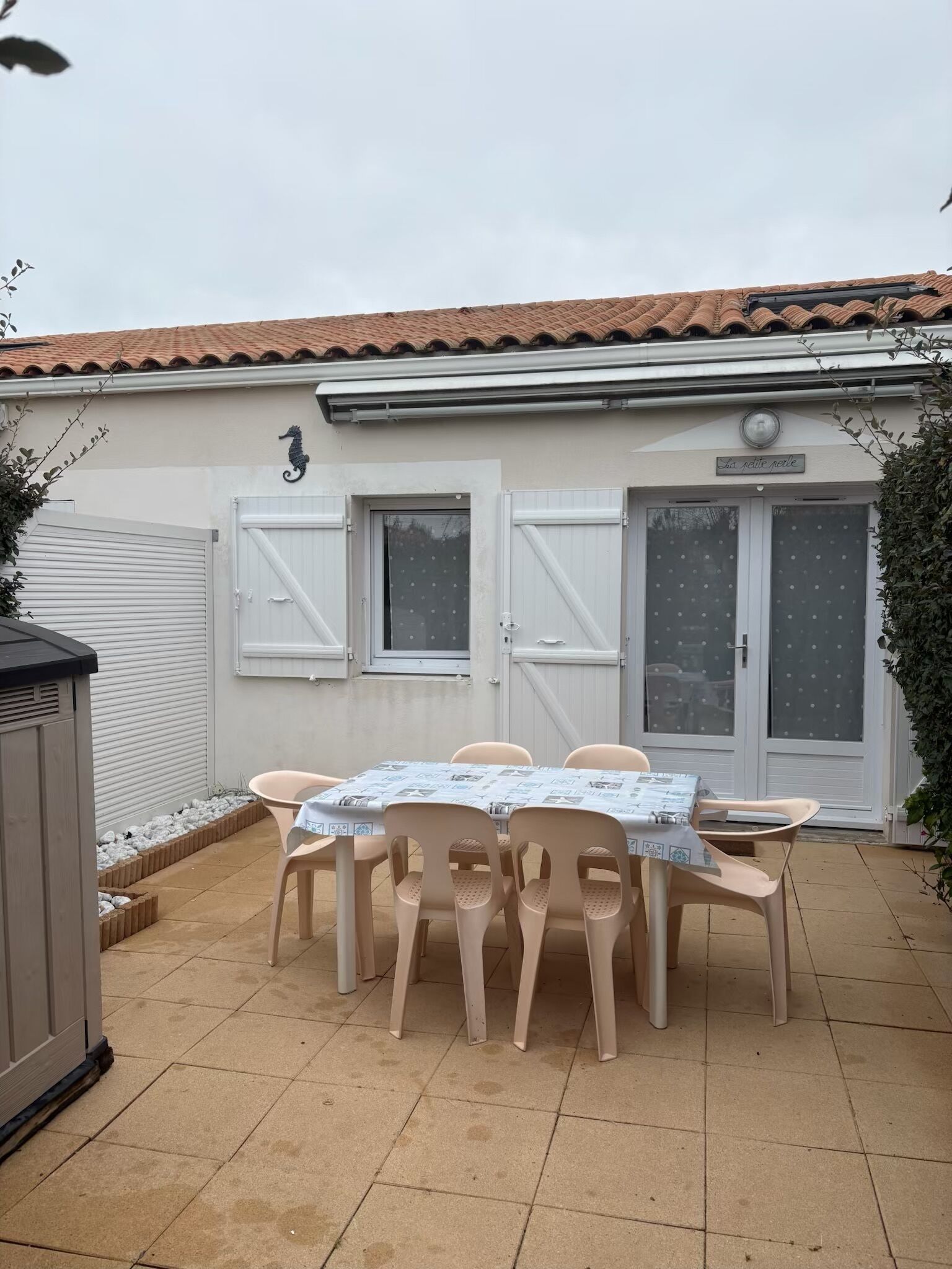Un patio con una mesa y sillas, una puerta de garaje blanca y un edificio con techo de tejas.