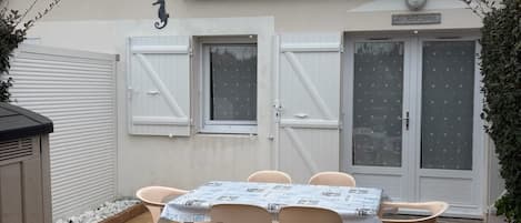 A patio with a table and chairs, a white garage door, and a building with a tiled roof.
