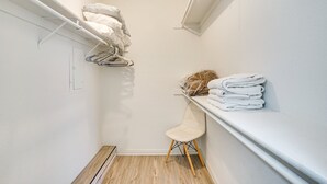 Een smalle inloopkast met een houten vloer, een witte stoel en een plank met opgevouwen handdoeken.
