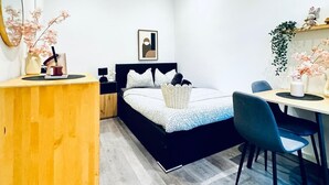 Een moderne slaapkamer met een bed, nachtkastje, bureau, stoel en een kleine plant.