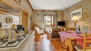 Una cuina acollidora amb fogó de gas, cadires de fusta, una taula de menjador amb camavela rosa i una paret de pedra.