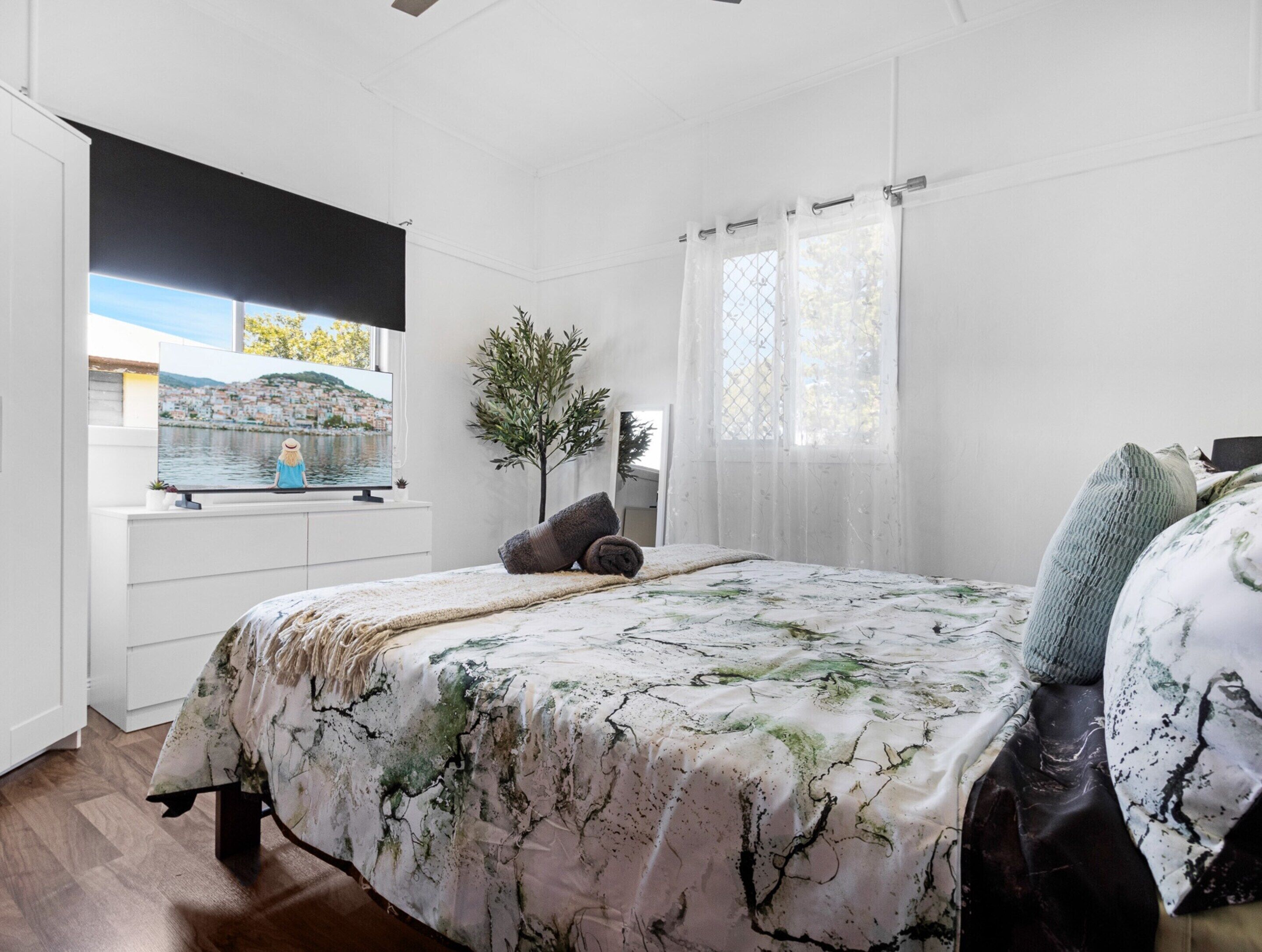 Un dormitorio con cama, televisor, ventana y vista a un pueblo, además de una planta.