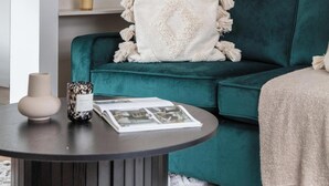 Ein blaugrünes Sofa mit weißer Decke, ein runder Couchtisch mit Dekoration und eine weiße Regaleinheit mit verschiedenen Gegenständen.