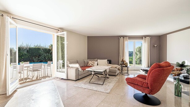 A spacious living room with a sofa, a red armchair, and a coffee table. There is a glass door leading to a balcony with outdoor furniture. - Quiet House With Pool (Biot)
