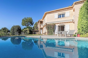 A swimming pool with lounge chairs, a building with a balcony, and surrounding greenery. - Quiet House With Pool (Biot)