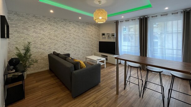 A modern living room with a grey sofa, a wooden dining table, and a TV. - Modern apartment - Railway station - City center (Le Mans)