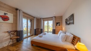 Een slaapkamer met een houten bed, een stoel, een tafel met een lamp en een schilderij aan de muur.