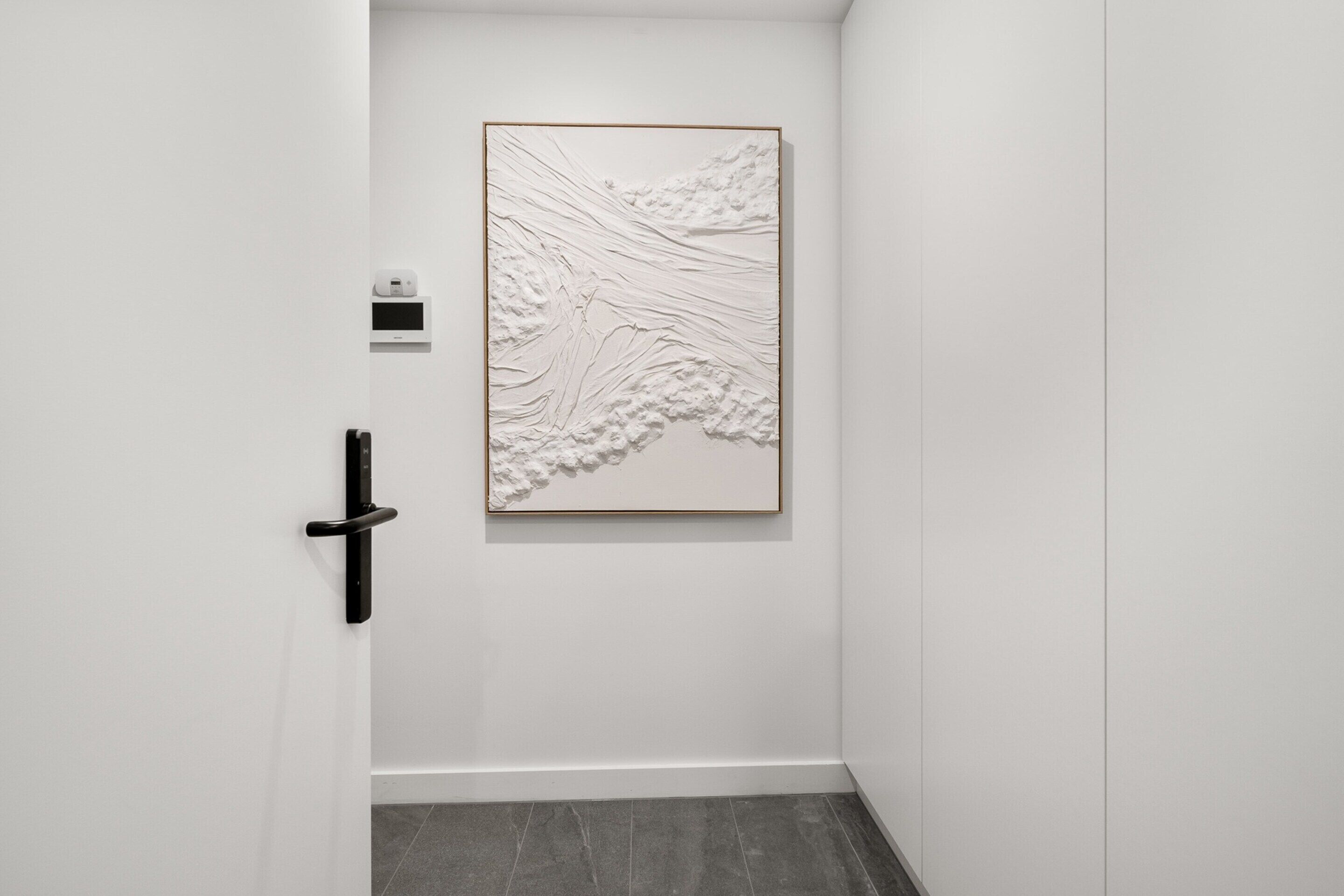 A hallway with a textured wall art piece, a door handle, and a small device on the wall.