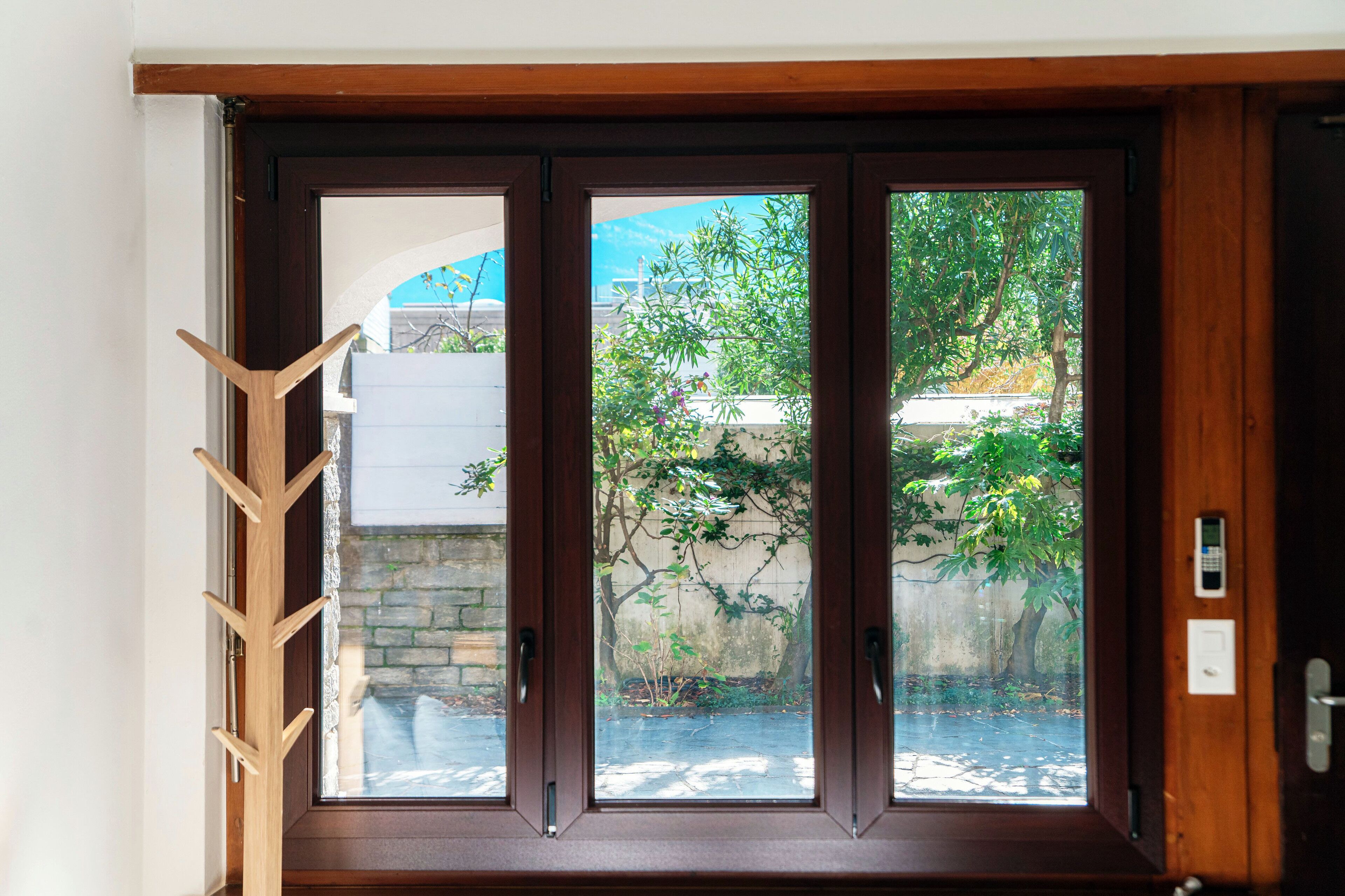A wooden door with a glass panel, a wooden coat rack, and a stone wall visible through the glass.