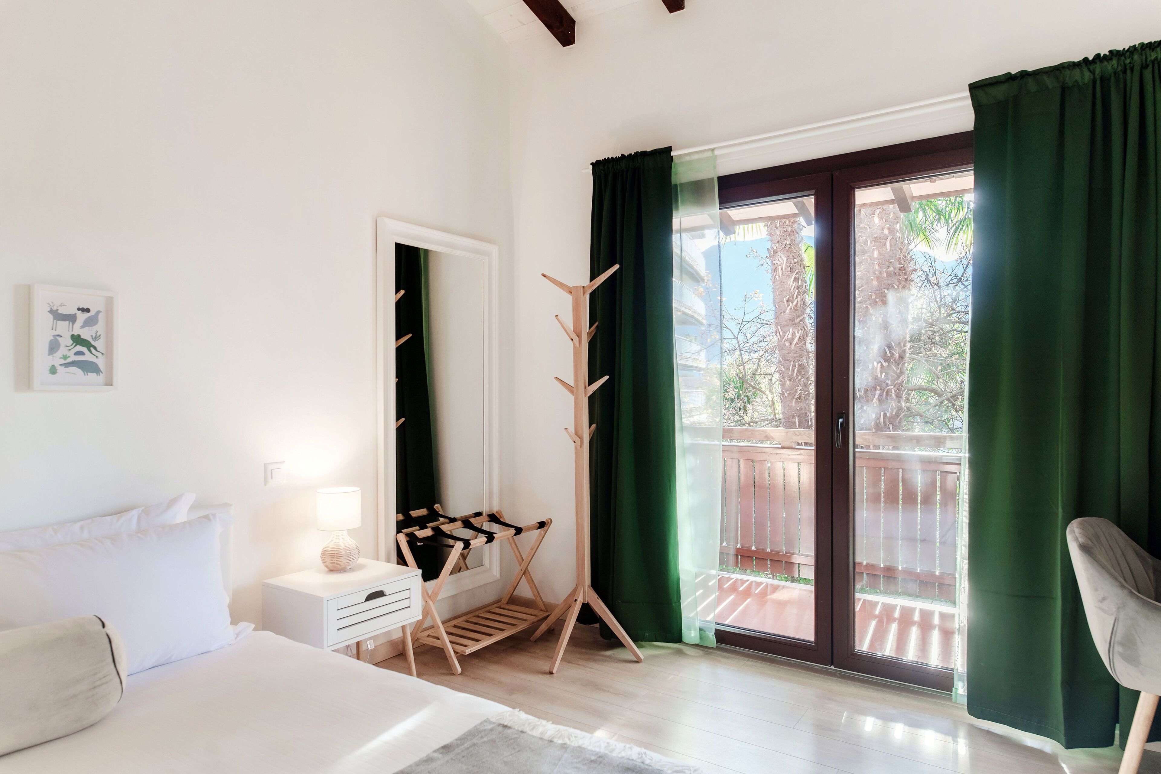 A bedroom with a bed, bedside table, lamp, drying rack, and a view of the outside balcony.