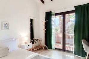 A bedroom with a bed, bedside table, lamp, drying rack, and a view of the outside balcony. - Florida Ascona Rooms (Ascona)