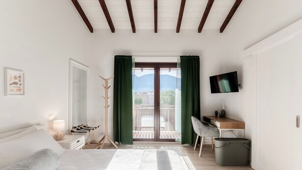 A bedroom with a bed, a desk, a TV, and a balcony with a view of the mountains. - Florida Ascona Rooms (Ascona)
