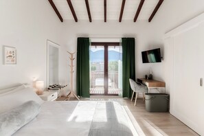 Ein Schlafzimmer mit Bett, Schreibtisch, Fernseher und einem Balkon mit Bergblick.