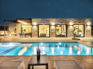 Un edificio moderno con piscina, asientos exteriores y una silla colgante.