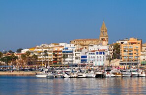 A marina with numerous boats docked, a prominent church with a bell tower, and colorful buildings along the waterfront. - Calma de Mar - Private Terrace, Air Conditioning, Wi-Fi - 6 minutes from the ocean - Ideal for families (Palamós)
