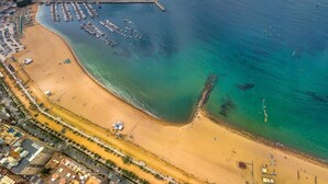 Luchtbeeld van een kustgebied met een zandstrand, een jachthaven met boten en een weg parallel aan het strand.