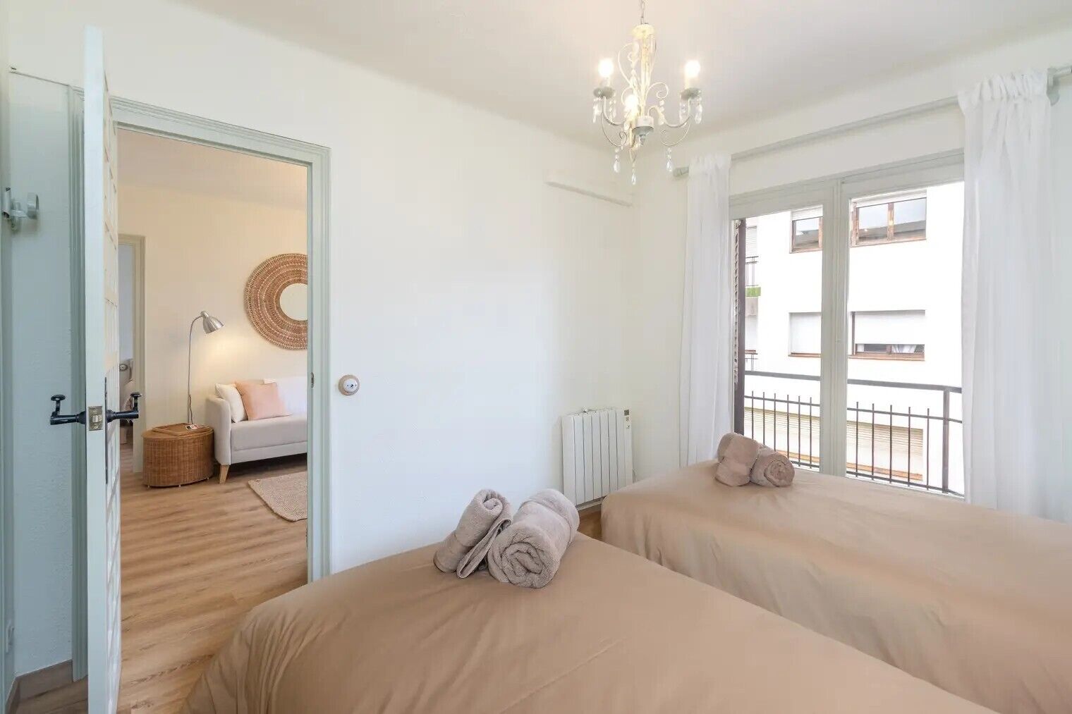 Ein Hotelzimmer mit zwei Betten, einer Chandelüster, Blick auf den Balkon und einer runden Wanddekoration aus Bändern.