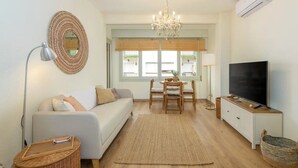 Een woonkamer met een bank, televisie, een kroonluchter en een eettafel met stoelen.
