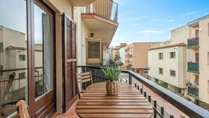 Een balkon met een houten tafel en stoelen, een bloempot en uitzicht op omliggende gebouwen.