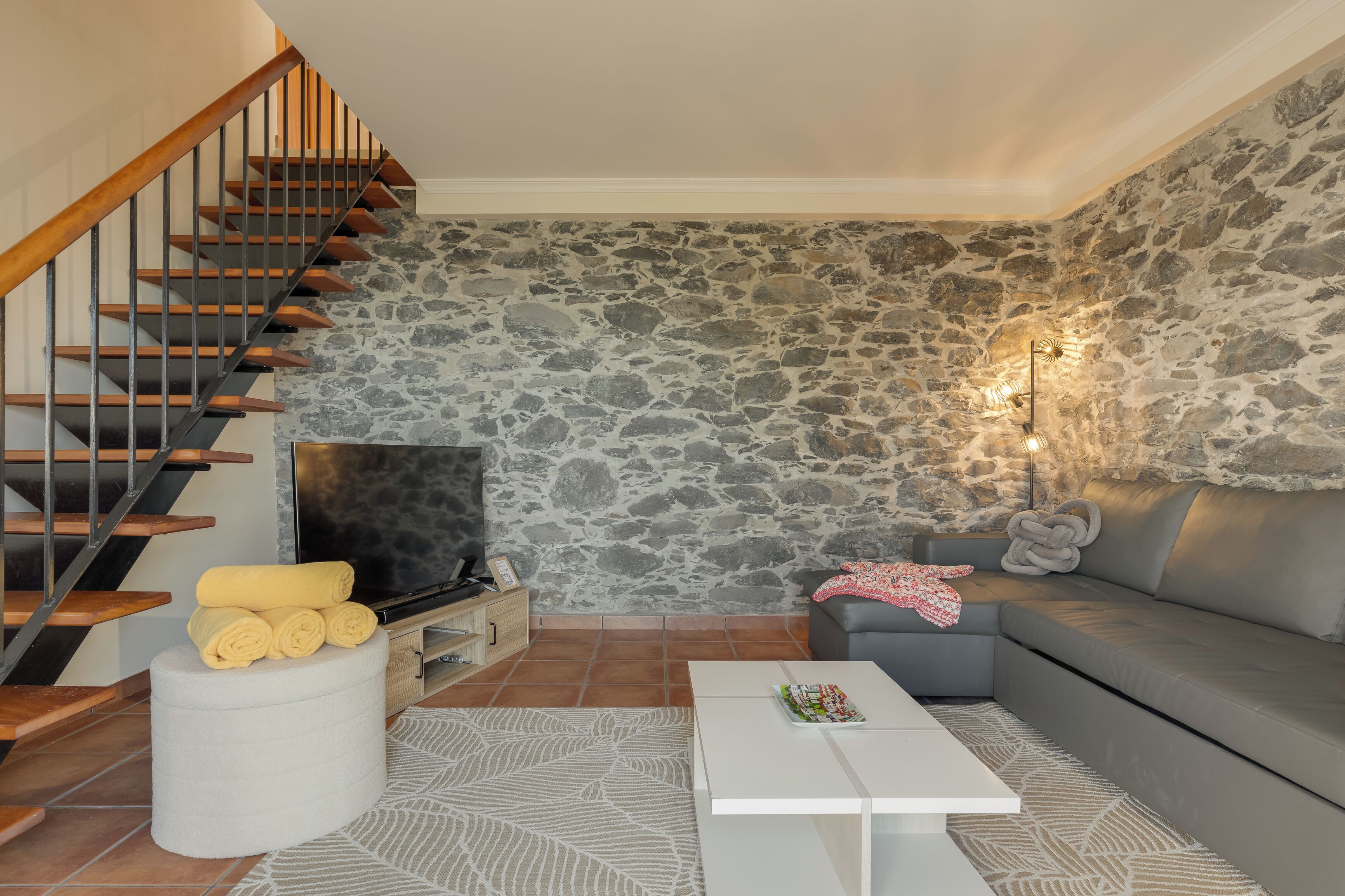 A modern living room with a stone wall, a sofa, a coffee table, and a staircase.