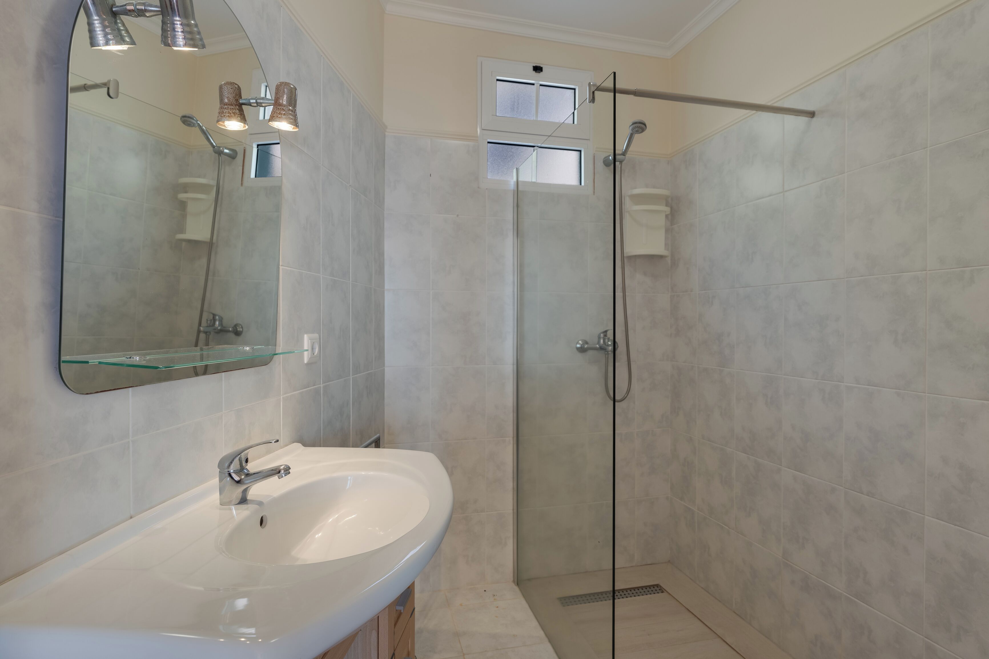 A modern bathroom with a glass shower enclosure, a white sink, and a large mirror.