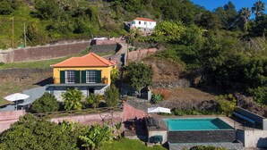A hillside property with a swimming pool, a yellow building with green shutters, and a white building in the background. - Casa Laranja by HR Madeira (Tabua)