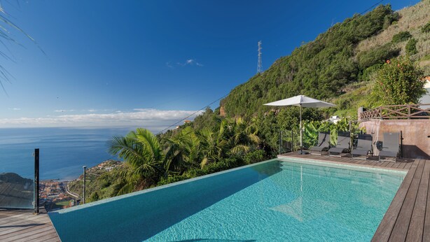 A swimming pool with a wooden deck, surrounded by lush greenery and overlooking a coastal view. - Casa Laranja by HR Madeira (Tabua)