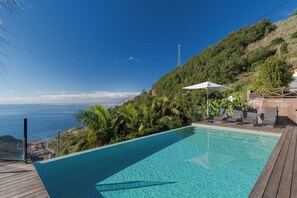 Une piscine dotée d’une terrasse en bois, entourée d’une végétation luxuriante et offrant une vue imprenable sur la côte.