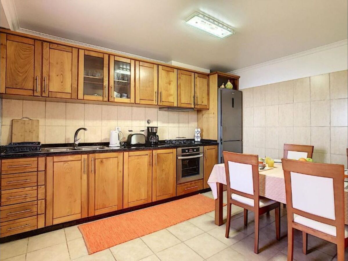 Una cocina con armarios de madera, una estufa, un refrigerador y una mesa de comedor con sillas.