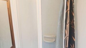 Ein Badezimmer mit weißem Waschbecken, einem Spiegel und einer Dusche mit Vorhang aus Bambusmuster.