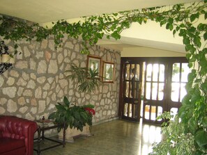 A room with a stone wall, a wooden door, a red leather sofa, and various potted plants. - Central Beachfront Apartment Next to the Marina (Marbella)