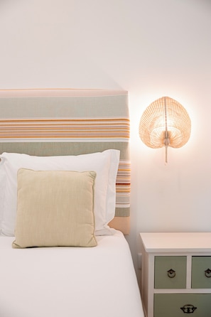 A neatly made bed with white and beige pillows, a striped headboard, and a wall-mounted lamp. - Quinta das Essencias (Penafiel)