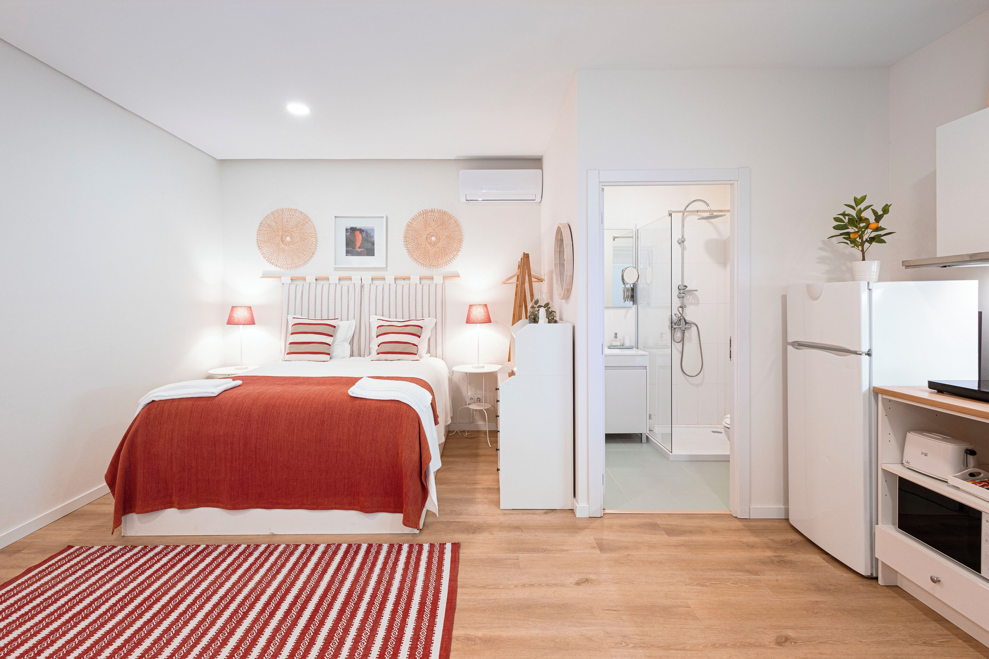 A modern bedroom with a bed, bedside lamps, a radiator, and a view into the bathroom.
