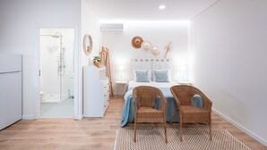 A modern bedroom with a bed, two wicker chairs, a bedside table, a lamp, and a wall-mounted hat rack. - Quinta das Essencias (Penafiel)