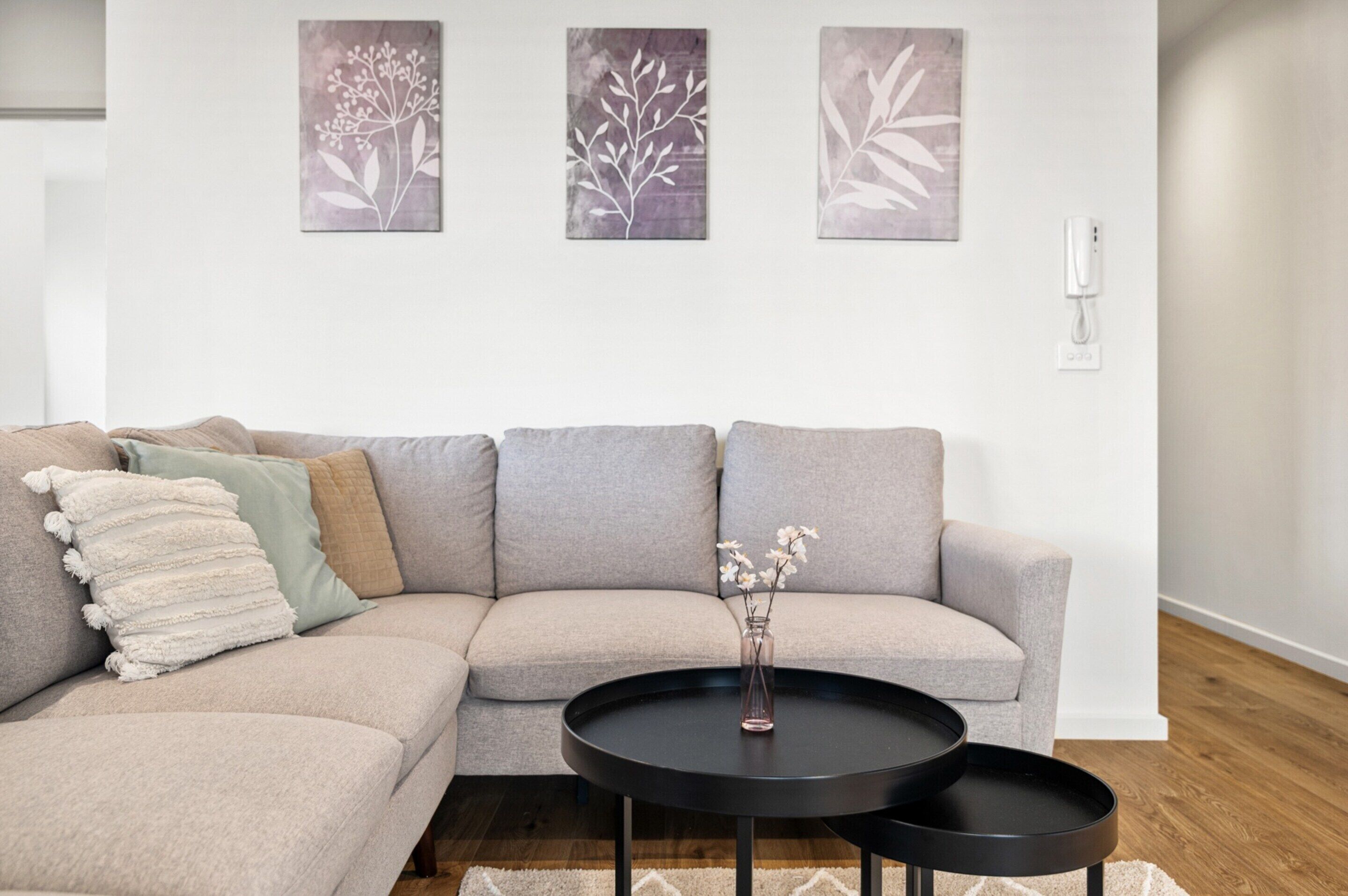 A modern living room with a sectional sofa, a round coffee table, and three wall-mounted artworks.