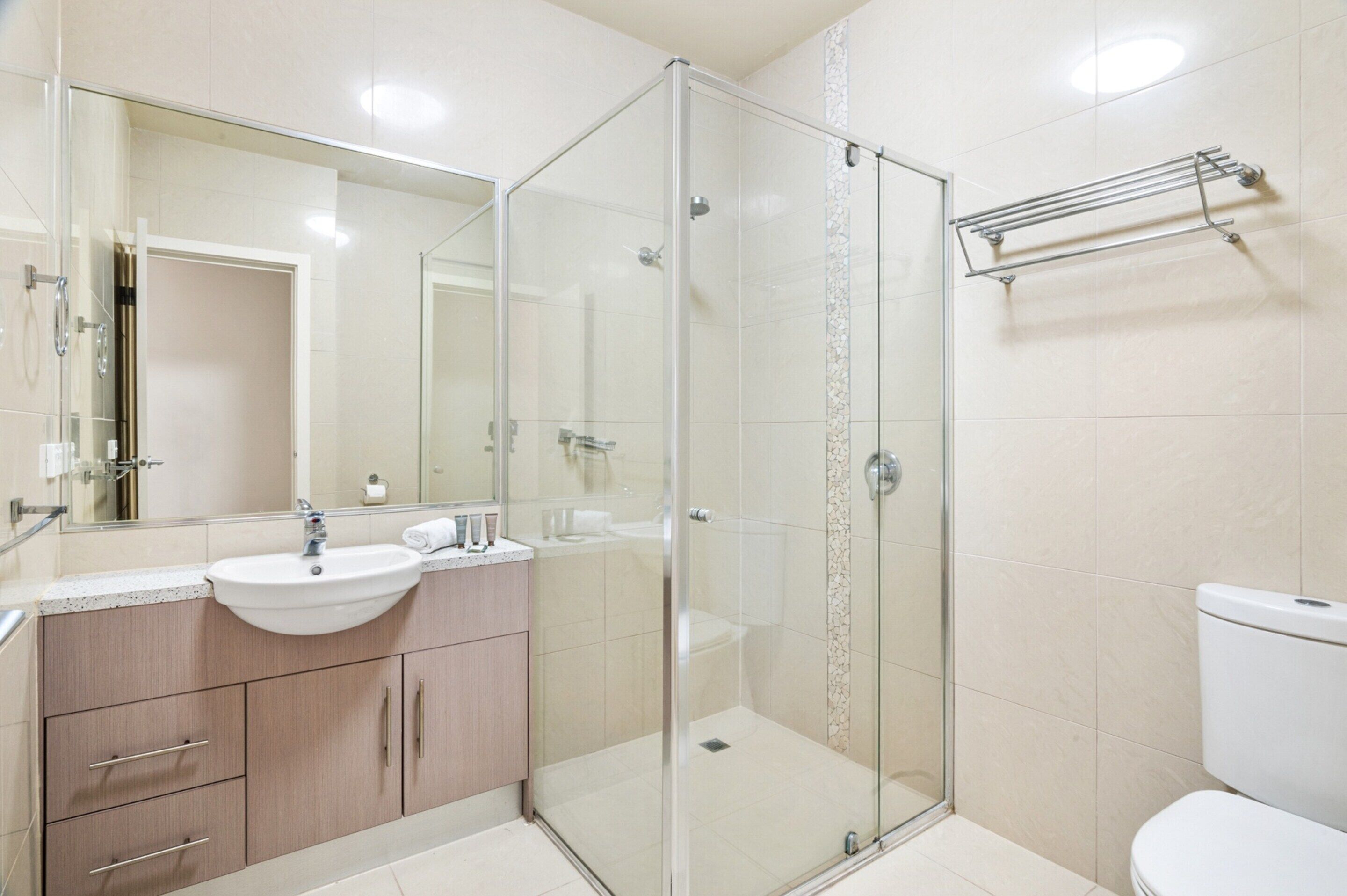 A modern bathroom with a glass shower enclosure, a sink with a mirror, and a towel rack.