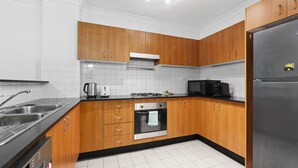 A modern kitchen with wooden cabinets, stainless steel appliances, and white tiled flooring. - Bright Marrickville Flat With Balcony & Parking (Sydney)