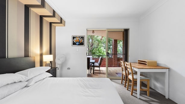 A modern hotel room with a bed, a desk, and a balcony with outdoor seating. - Bright Marrickville Flat With Balcony & Parking (Sydney)