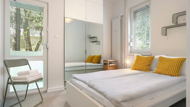 A modern bedroom with a bed, a chair with towels, and a window with blinds. - Starflat Cozy central apartment NDK (Sofia)