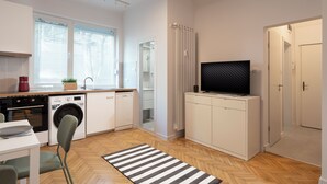 A compact kitchen with a washing machine, a dining table, and a TV on a cabinet. - Starflat Cozy central apartment NDK (Sofia)