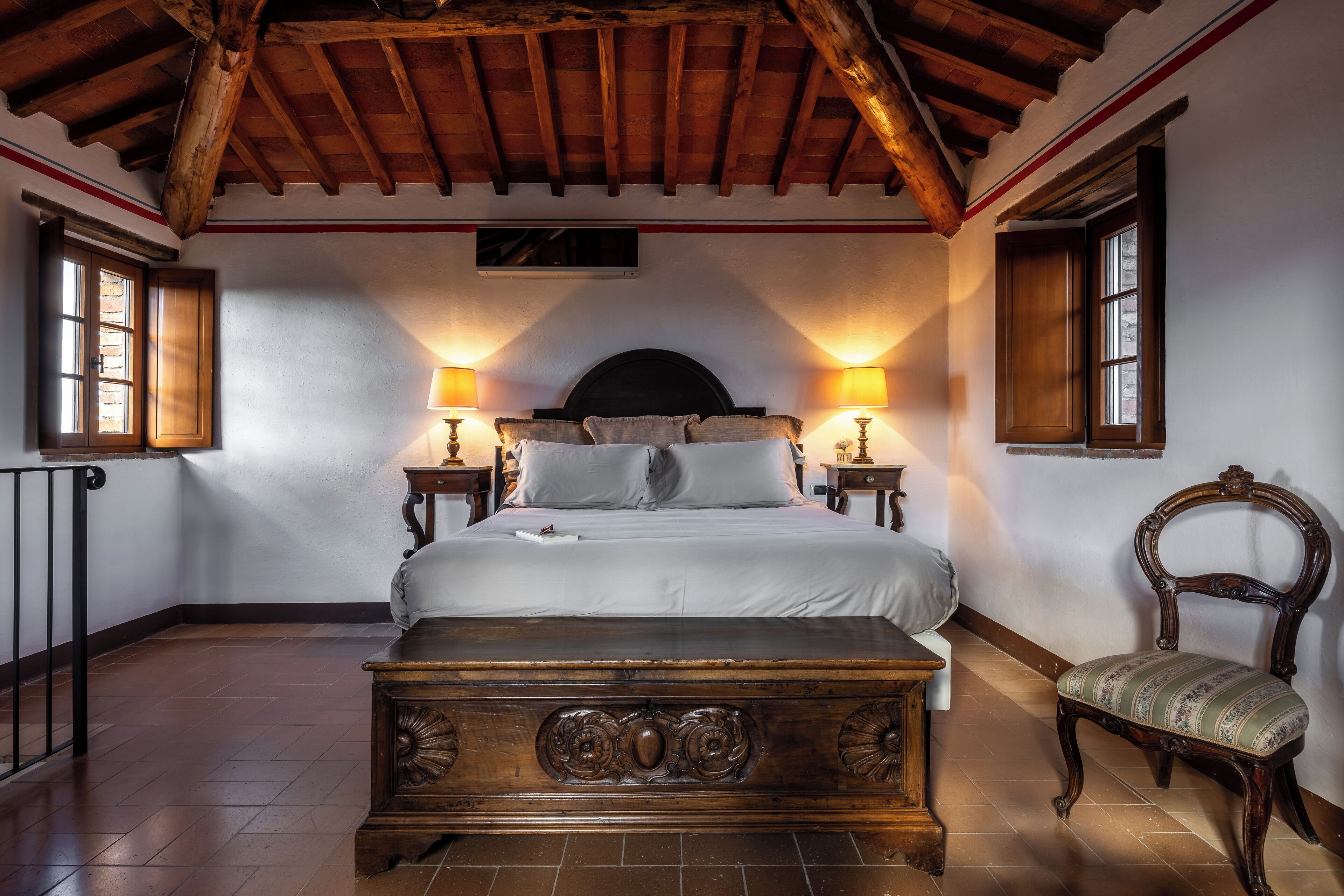 A bedroom with a wooden bed, two bedside lamps, a chair, and a wooden ceiling.