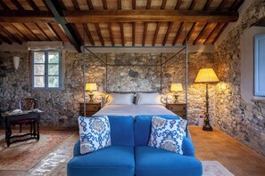 Une chambre avec un mur en pierre, un lit à baldaquin et un canapé bleu.