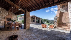 An outdoor patio with stone flooring, wooden furniture, and a stone wall. -  Il Gabbro Luxury by Geco Vacation Rentals (Casole d'Elsa)