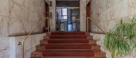 A marble staircase with red carpeted steps, flanked by marble walls and gold handrails.