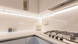 Een moderne keuken met een gasfornuis, witte kastjes en verlichting onder de kast.