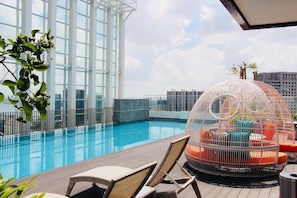 Zona de piscina en la azotea con vistas despejadas del horizonte de la ciudad, una estructura de vidrio y una silla de descanso con forma de pájaro.
