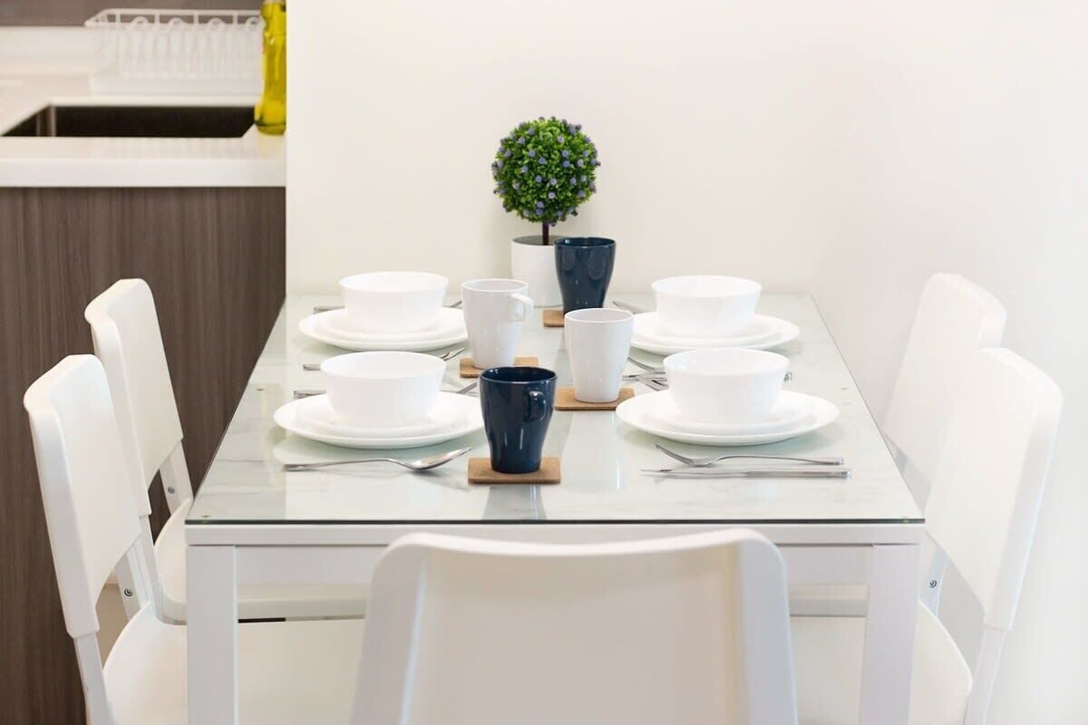 A dining table set with white plates, cups, and a blue mug, surrounded by white chairs.