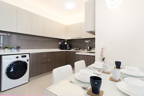 Una cocina moderna con lavadora integrada, armarios de madera y comedor con sillas y platos blancos.